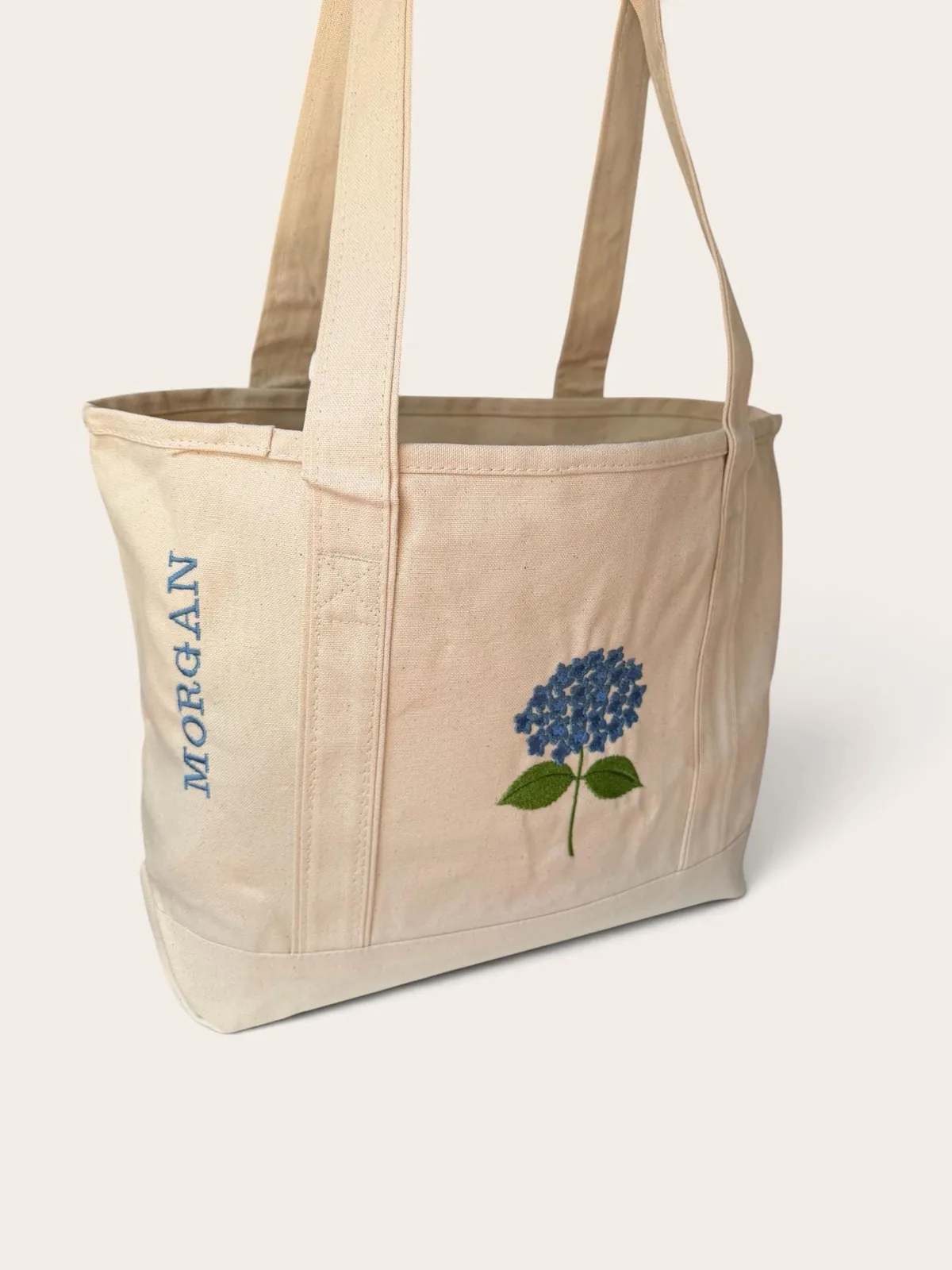 Canvas tote with a blue embroidered hydrangea and MORGAN stitched down the side